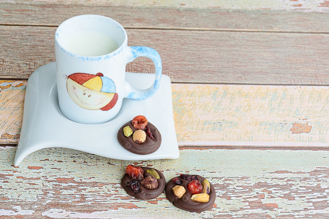 Biscoitos de chocolate com nozes ao lado de uma pequena caneca de leite.