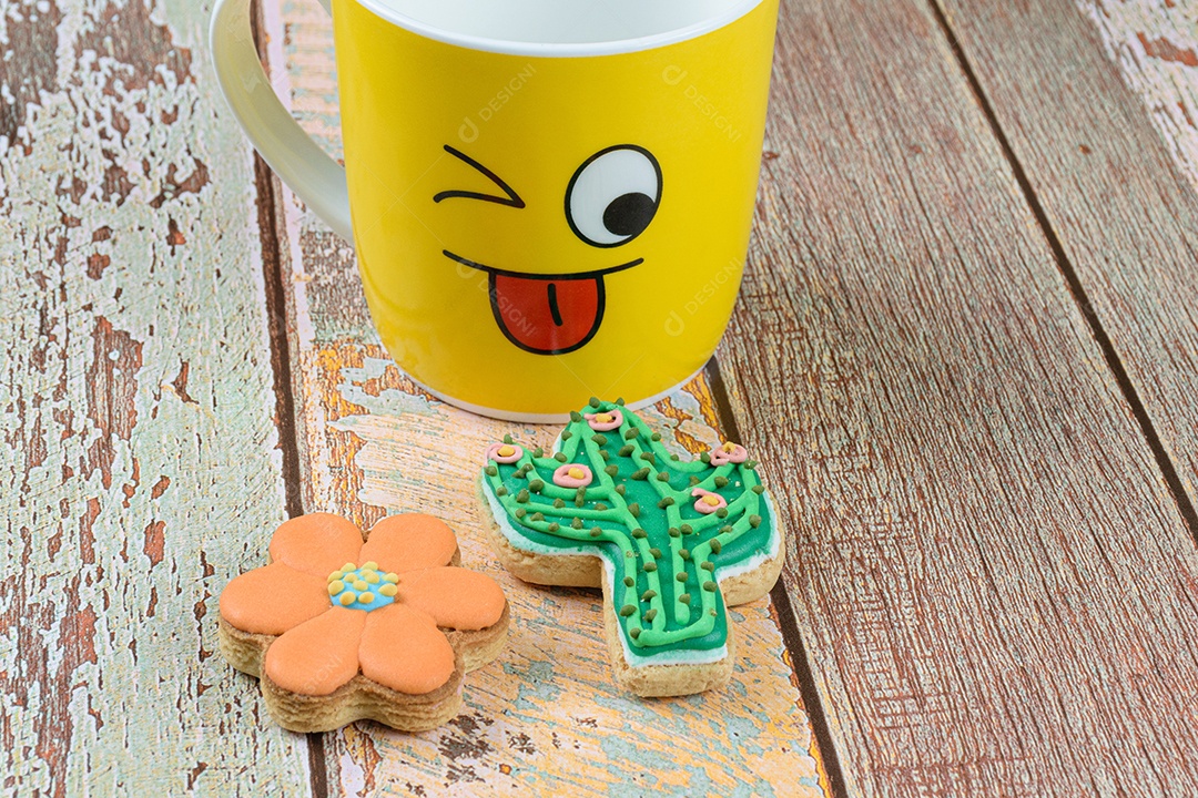 Biscoitos de flores e cactos, ao lado de uma caneca amarela