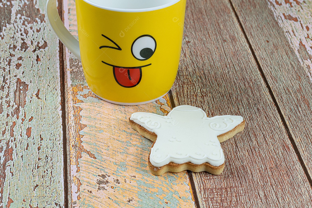 Biscoito em forma de anjo em uma mesa de madeira, ao lado de um show de caneca amarela