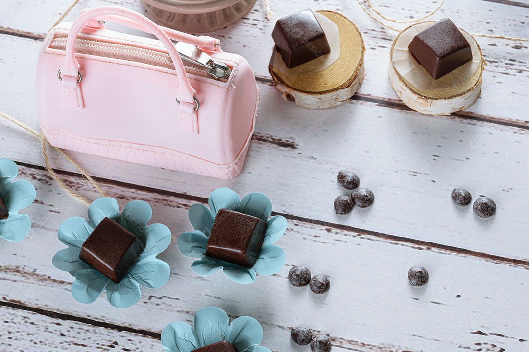 Bombons de chocolate ao lado de um saquinho rosa e callets de chocolate