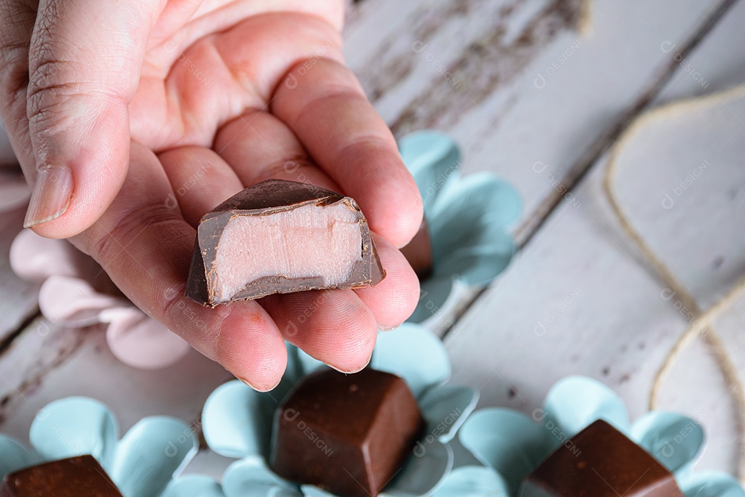 Mão segurando um bombom de chocolate cortado ao meio, mostrando ganache rosa