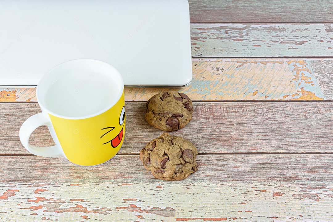 Biscoitos de gotas de chocolate cercados por uma caneca amarela com leite