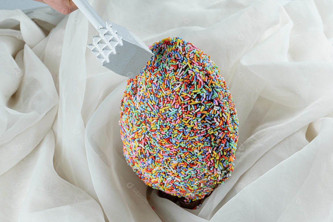 Mão de uma mulher com um martelo preparado para quebrar o ovo de Páscoa