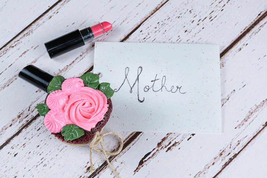 Cupcake red velvet com cobertura de creme de manteiga, ao lado de um batom