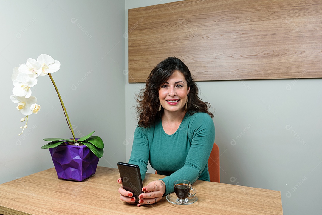 Mulher brasileira, sorridente e tatuada, com smartphone nas mãos