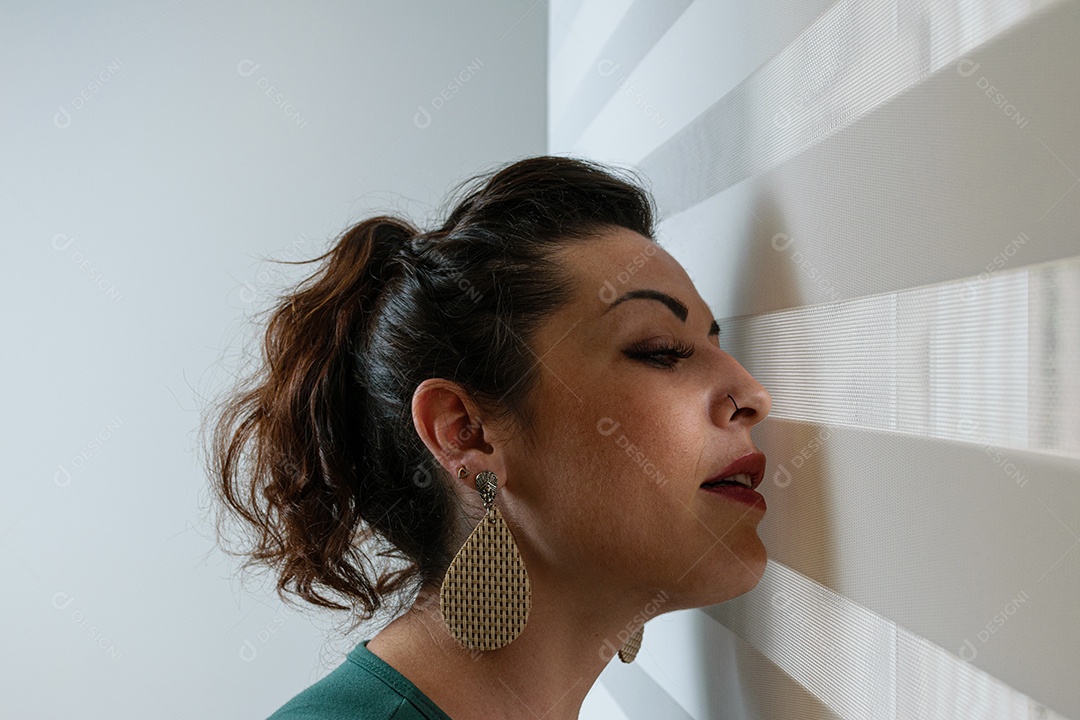 Mulher brasileira de 35 anos olhando a rua através da cortina.