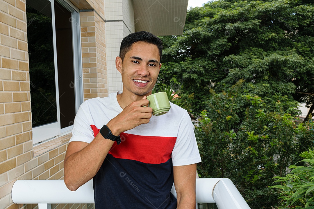 Sorridente jovem brasileiro segurando uma xícara de café na varanda