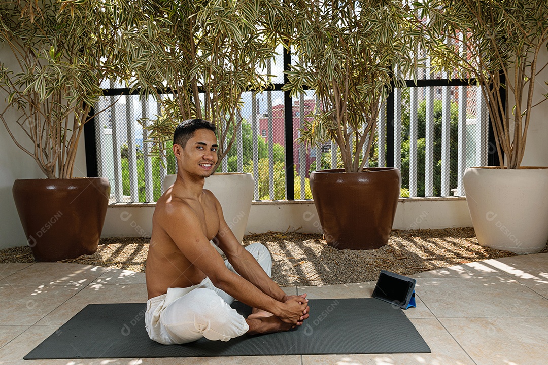 Jovem brasileiro sorridente, fazendo aula de ioga online