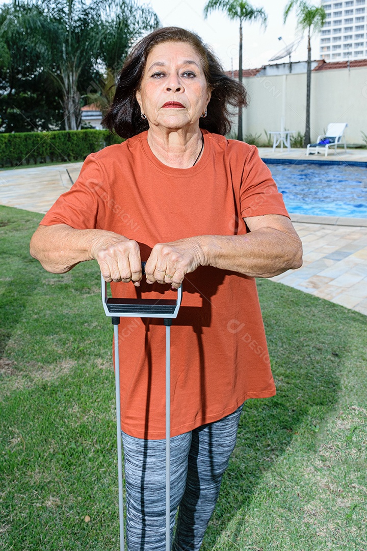 Mulher de 74 anos fazendo exercícios com elástico na beira da piscina.