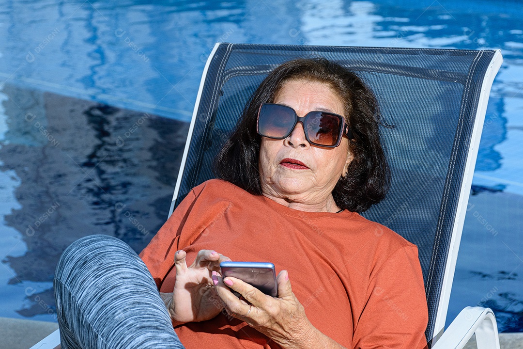 Detalhe de uma mulher de 74 anos sentada em uma espreguiçadeira e usando celular
