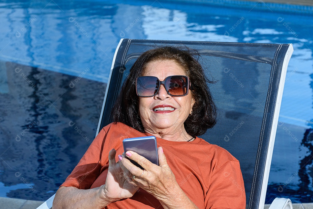 Detalhe de uma mulher de 74 anos sentada em uma espreguiçadeira e usando celular