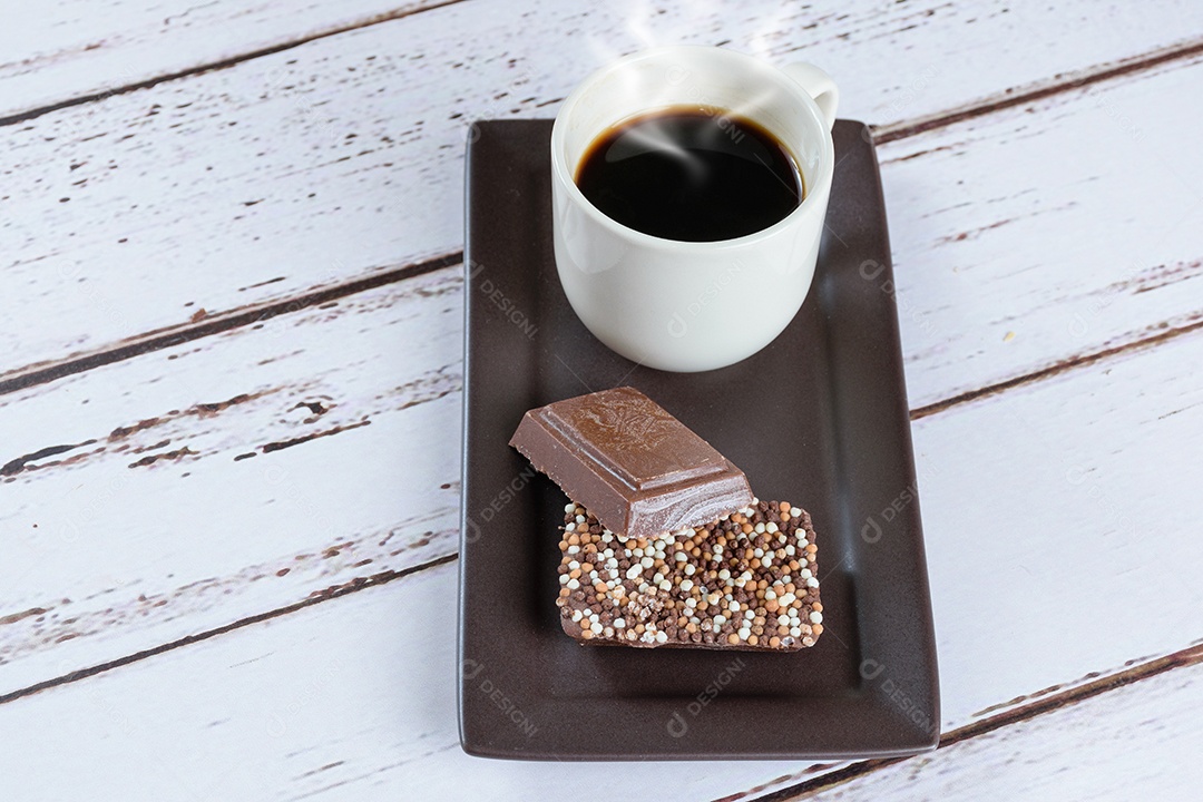 Barras de chocolate ao leite com granulado ao lado de uma xícara de café.