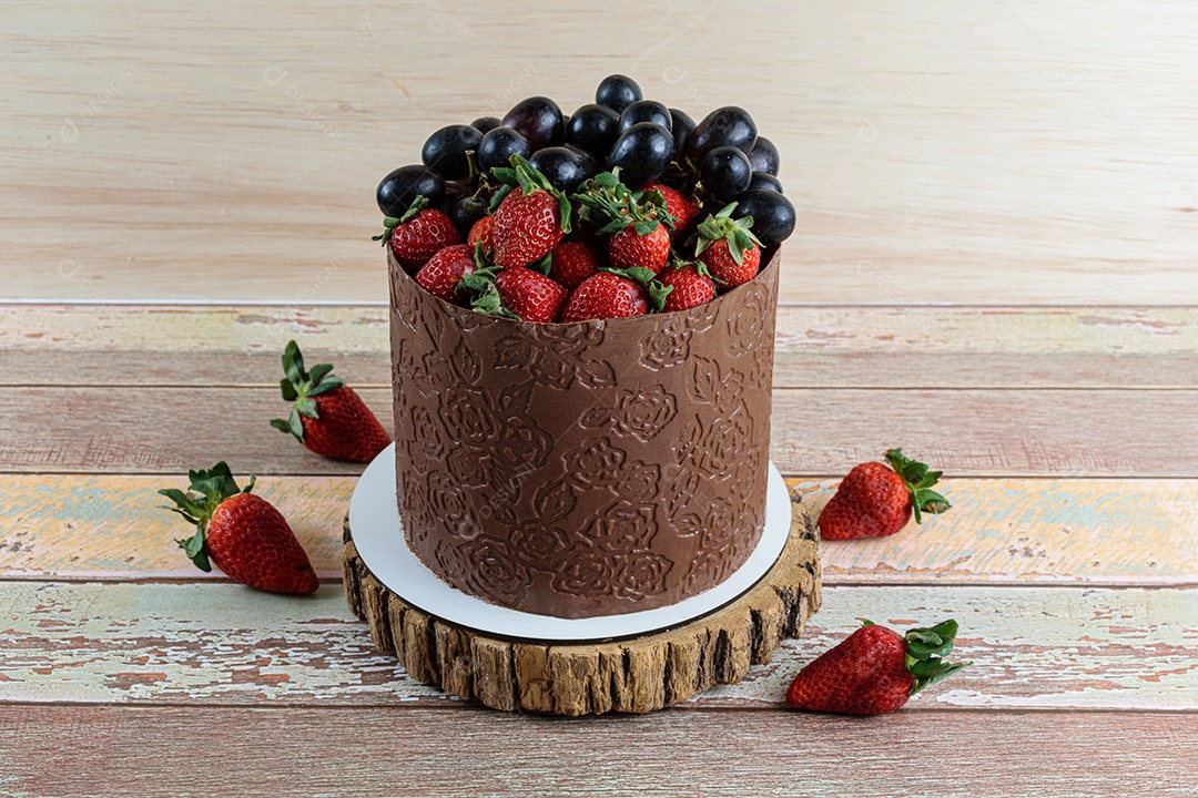 Bolo coberto de chocolate, decorado com uvas e morangos,