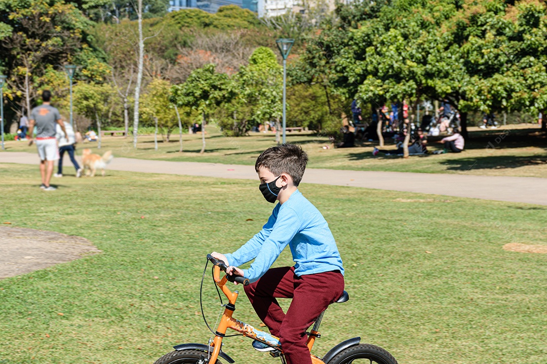 criança de 8 anos, em um dia ensolarado, andando de bicicleta em um parque público