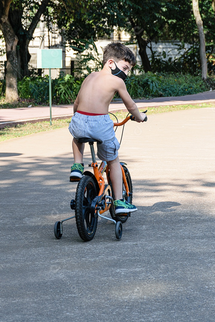 criança de 8 anos com máscara, sem camisa, andando de bicicleta