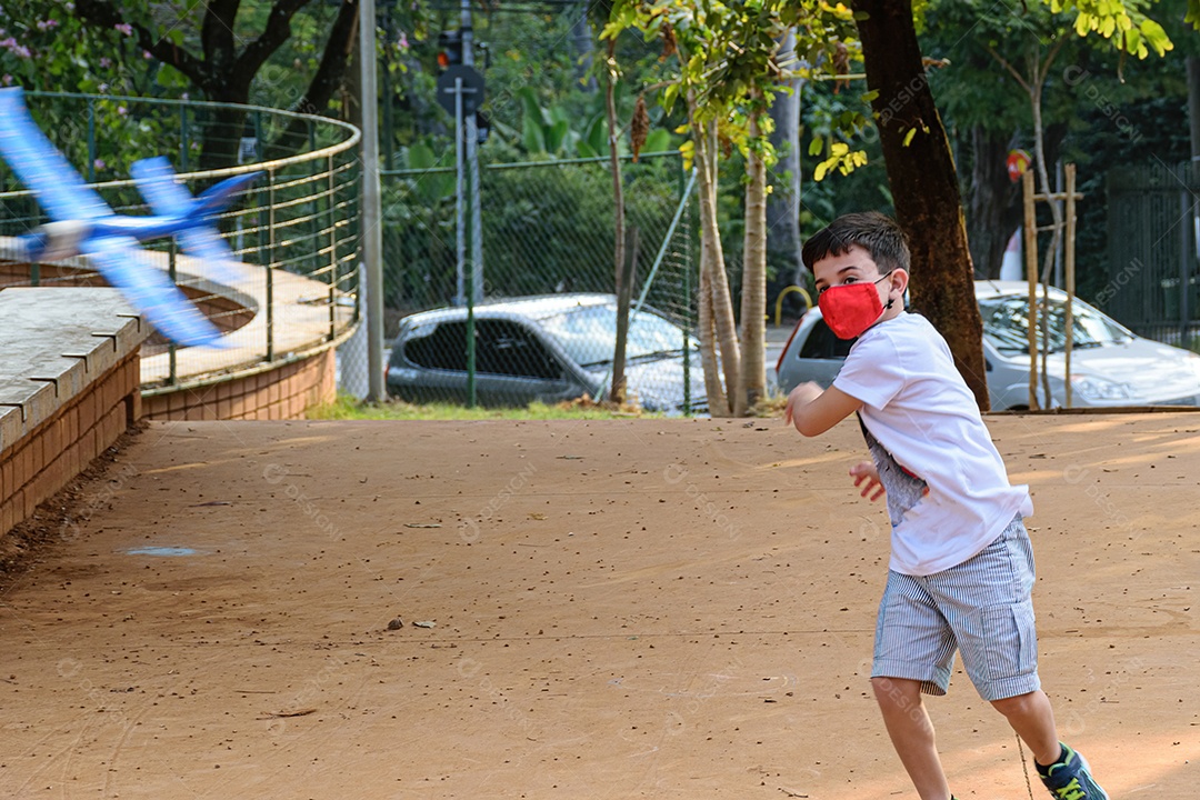 Criança de 8 anos, usando máscara, brincando com aviãozinho de isopor