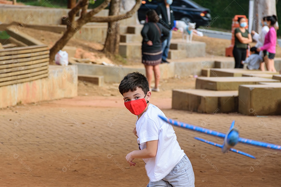 Criança de 8 anos, usando máscara, brincando com aviãozinho de isopor