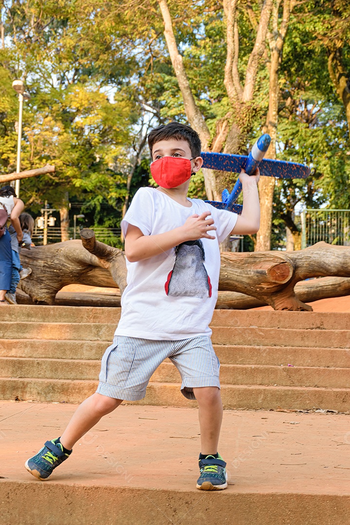 Criança de 8 anos com máscara jogando seu avião de isopor azul em um