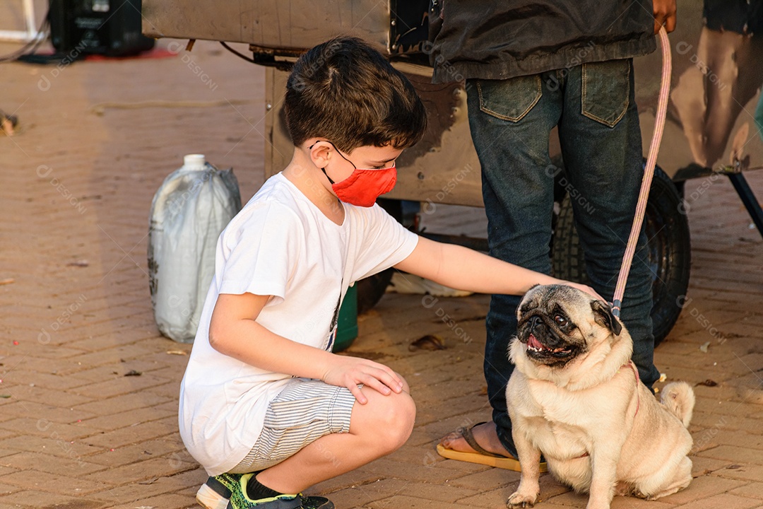 Criança de 8 anos, com máscara, agachada e acariciando um cão Pug.