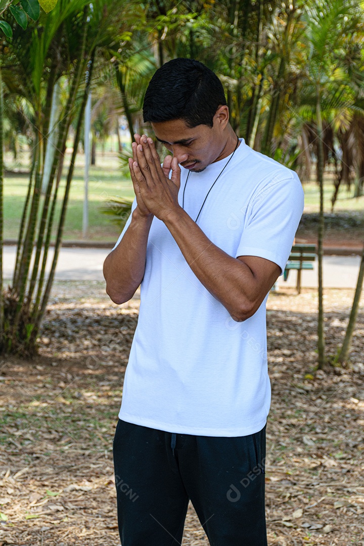 Jovem brasileiro em parque público, com as mãos próximas ao rosto