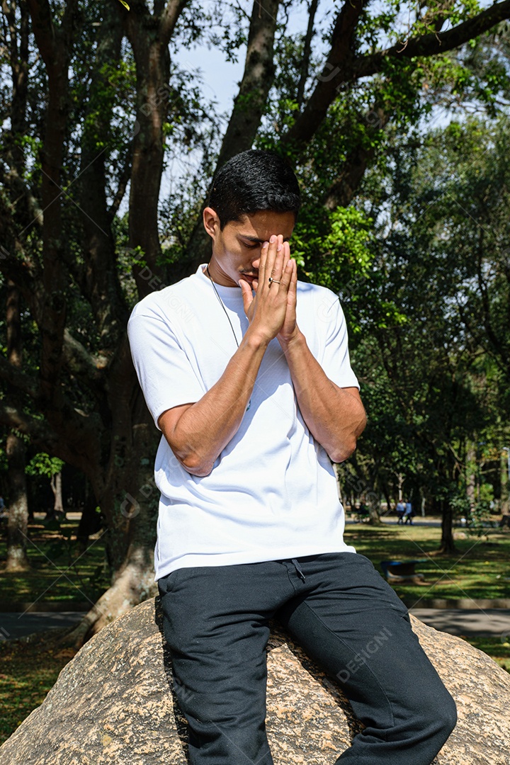 Jovem brasileiro encostado em uma pedra, com as mãos fechadas