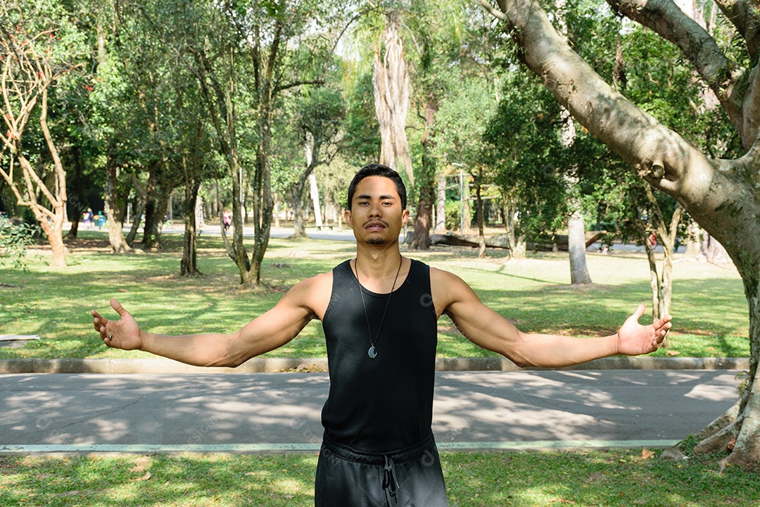 Jovem brasileiro, professor de ioga, de braços abertos em um parque público