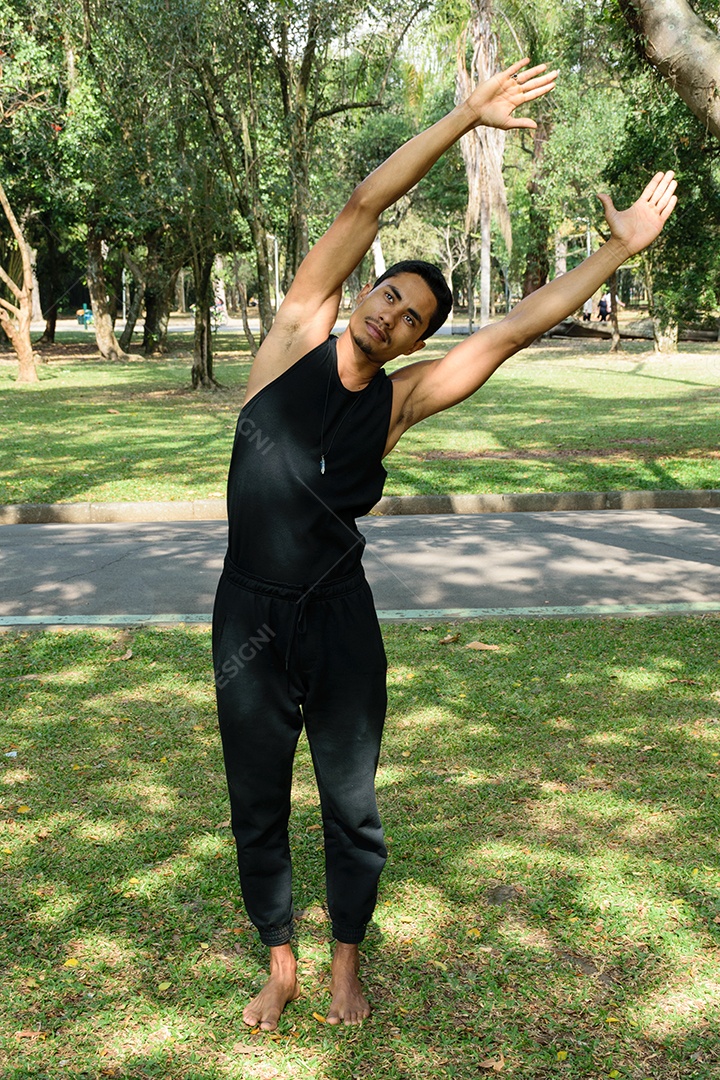 Jovem brasileiro, professor de ioga, fazendo alongamento em parque público