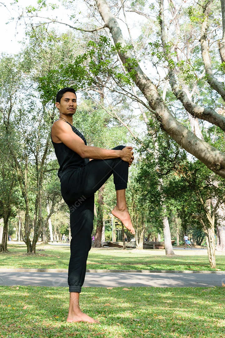 Jovem brasileiro puxando o joelho ao peito, em uma praça público