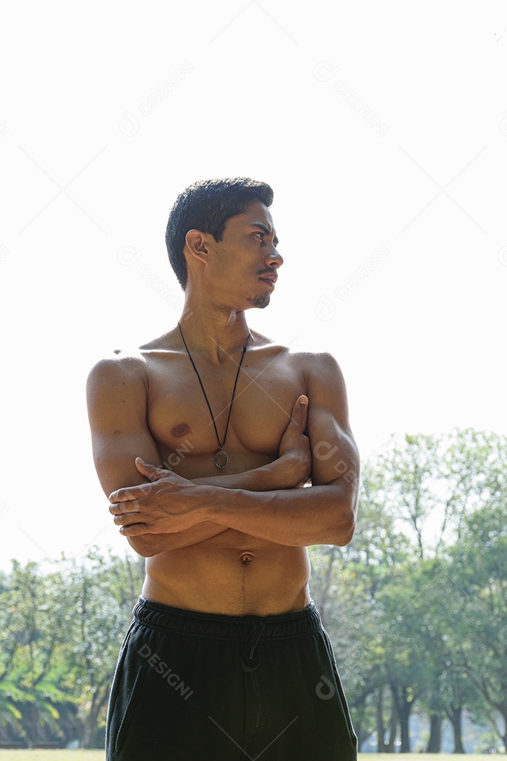 Jovem brasileiro sem camisa, braços cruzados, sendo iluminado por trás