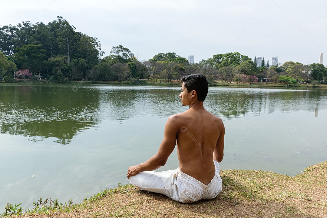 Jovem brasileiro sentado de costas na beira de um lago