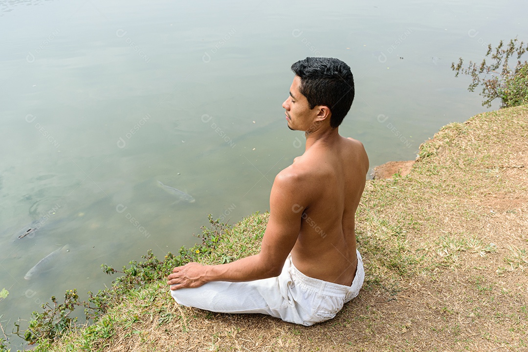 Jovem brasileiro sentado olhando para o lago em meditação
