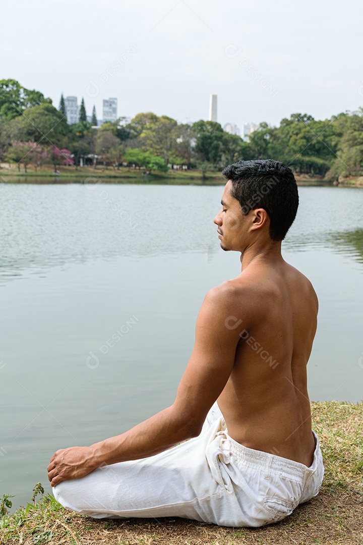 Jovem brasileiro sentado olhando para o lago em meditação