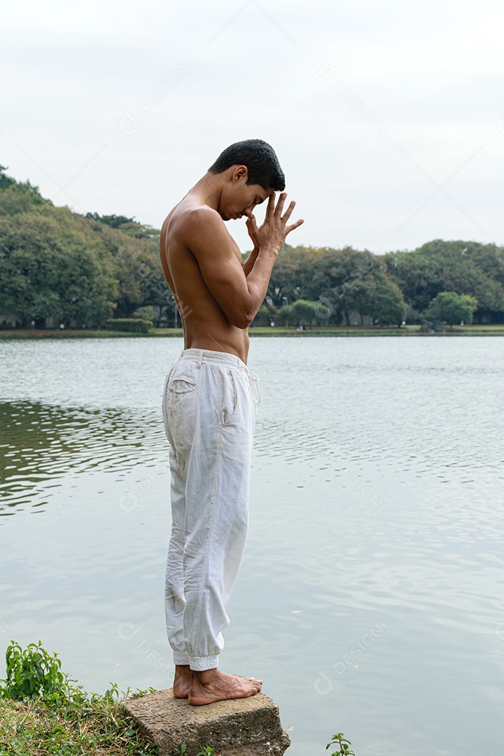 Jovem brasileiro parado ao lado de um lago em uma posição agradecida