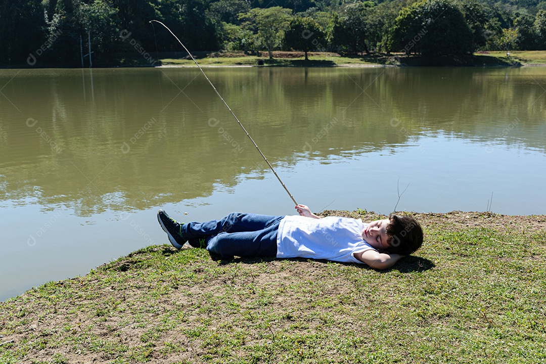 Criança brasileira de 8 anos, deitada e pescando no lago