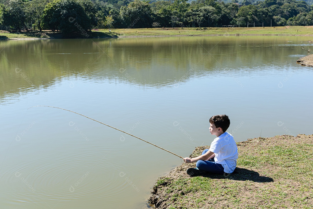 Criança brasileira de 8 anos, sentada à beira do lago