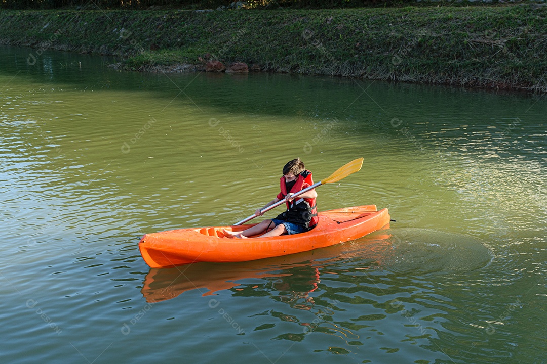 Criança brasileira de 8 anos aprendendo a usar um caiaque em um pequeno rio