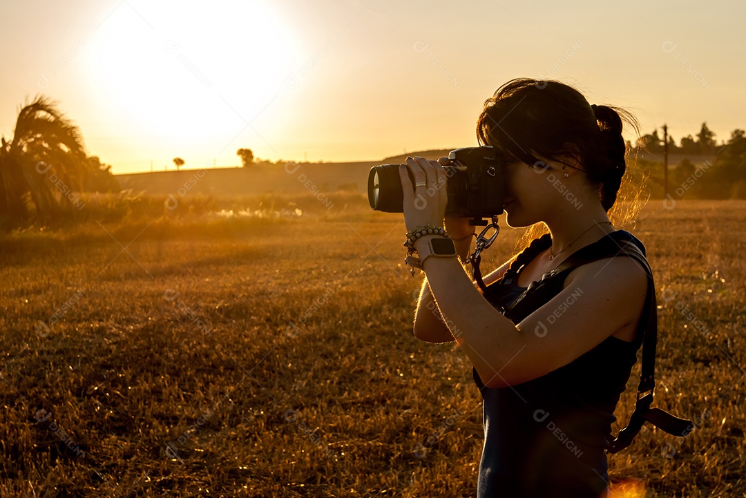Jovem mulher fotografando em um campo de soja ao pôr do sol