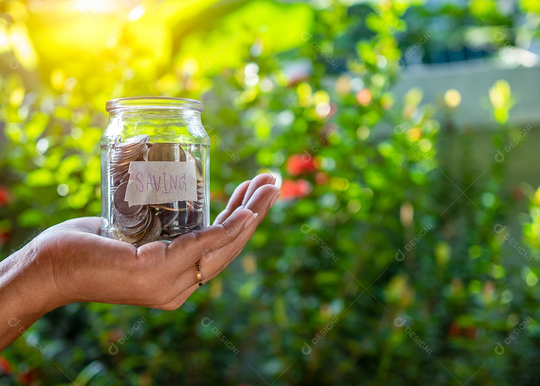 Mão humana e garrafa de cofrinho com sinal de poupança no fundo natural do bokeh.