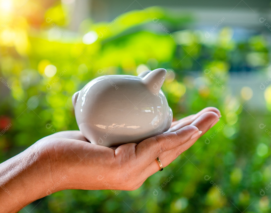 Mão humana e cofrinho no fundo natural do bokeh.