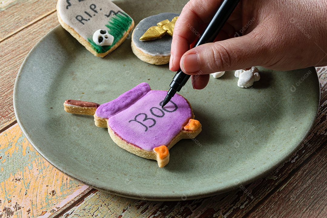 Confeiteiro escrevendo em um biscoito amanteigado roxo em forma de caldeirão