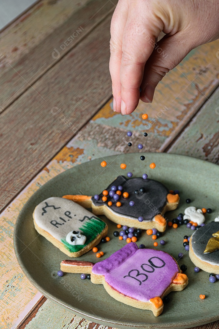 Biscoitos amanteigados temáticos de Halloween sendo decorados por uma confeiteira