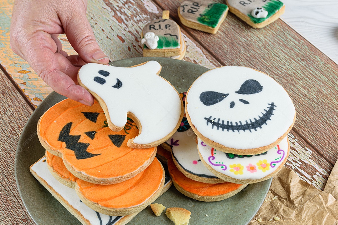 Mão feminina pegando um biscoito amanteigado com tema de Halloween