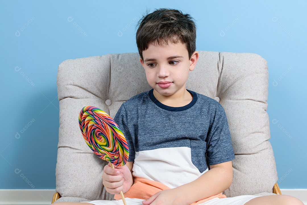 Brasileiro de 8 anos sentado na poltrona. Segurando e olhando pirulito