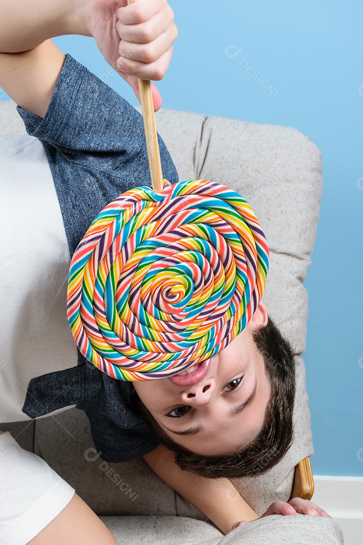 Criança brasileira de 8 anos segurando e mordendo um grande pirulito colorido