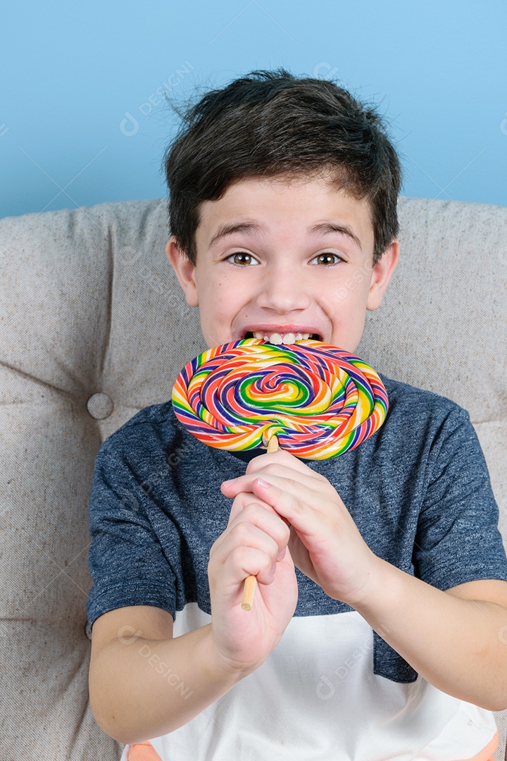 criança de 8 anos mordendo e sorrindo um grande pirulito colorido