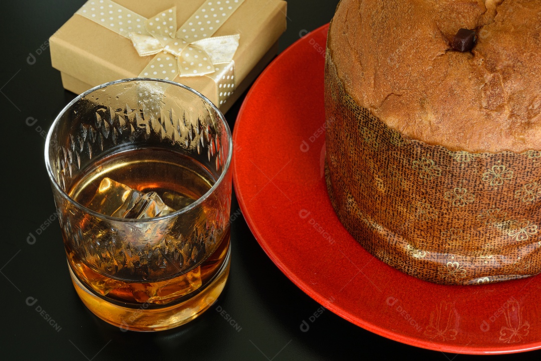 Copo com uísque e gelo ao lado de um panetone e uma caixa de presente