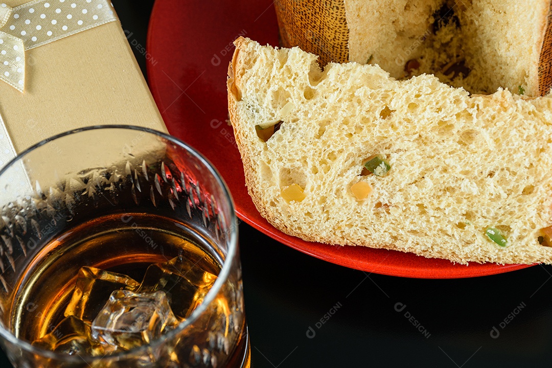 Detalhe de uma fatia de panetone ao lado de um copo com uísque