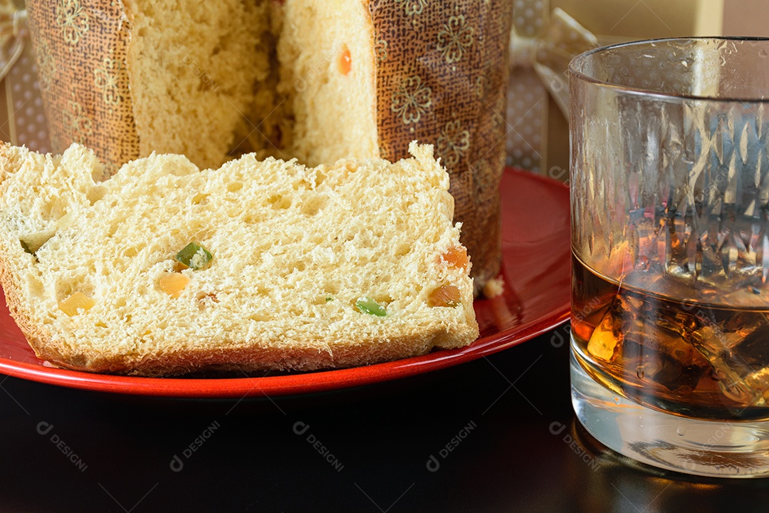 Detalhe de uma fatia de panetone ao lado de um copo de uísque