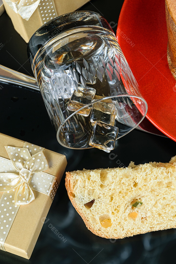 Fatia de panetone sob fumaça de cigarro, ao lado de caixa de presente e copo de uísque virado