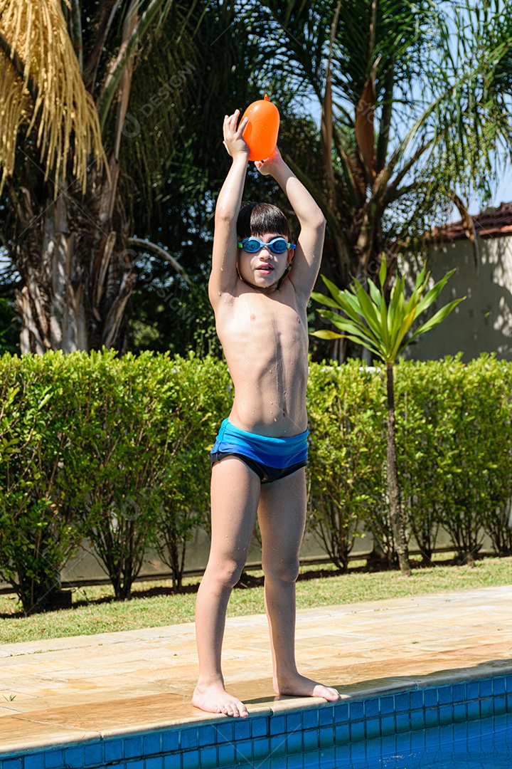 Criança de 8 anos com óculos de mergulho, com uma bomba dágua na cabeça na beira da piscina.